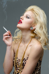 Obraz premium Portrait of young beautiful blond woman with red lips in the studio in a beautiful dress smoking a cigarette