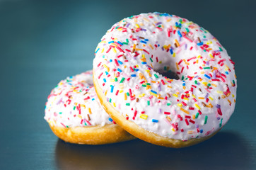 Donut with sprinkles and white iced. Donuts background. Cake and sweet. Food detail. Close up