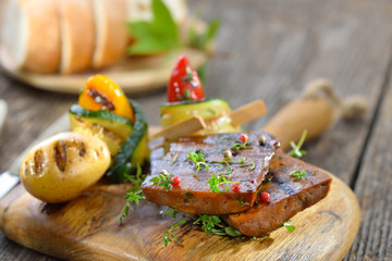 Vegan grillen: Grillteller mit Seitan dazu Zucchini-Röllchen, Grillkartoffel und Ciabatta serviert...
