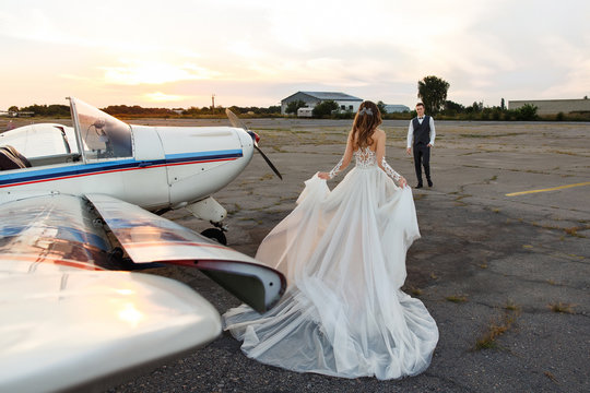 Beautiful bride in luxury wedding dress goes to meet the groom near the airplane