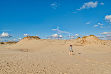 Fototapeta na wymiar Young redhead woman walking under sun along endless sandy dunes