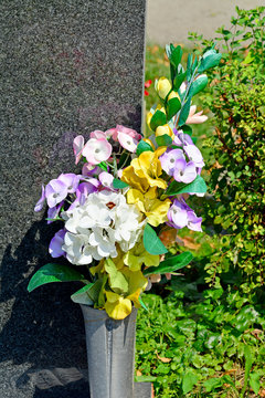 Kunstblumen mit Vase am Grabstein