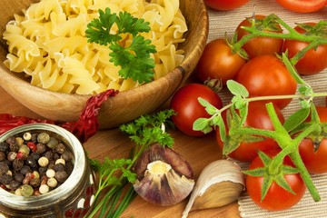 Raw pasta with tomatoes and parsley on a wooden background. Preparation diet food. The recipe for a simple dinner. Traditional pasta with vegetables.
