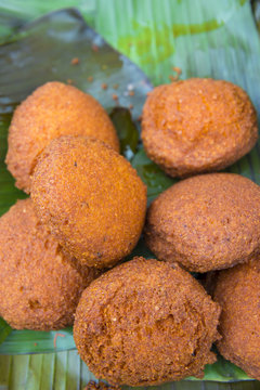Freshly cooked Brazilian acaraje balls piled on green banana palm leaves at an outdoor street food stall