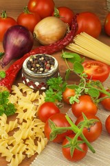 Raw pasta with tomatoes and parsley on a wooden background. Preparation diet food. The recipe for a simple dinner. Traditional pasta with vegetables.
