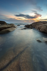 seascape with smooth wave, rock and sunset