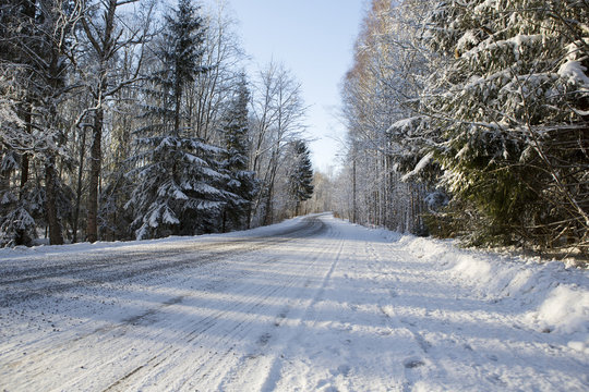 A slippery and curvy road in the winter. Image taken in Finland during sunrise on a cold morning. First snow is covering up the road and forest