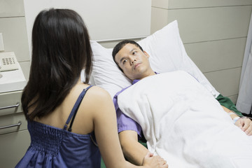 man a husband on bed as patient in hospital or clinic with woman a wife take care on hospital bed side with love and care