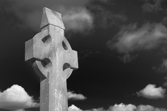 Old stone celtic cross on a bright sunny day with cloudy sky. 