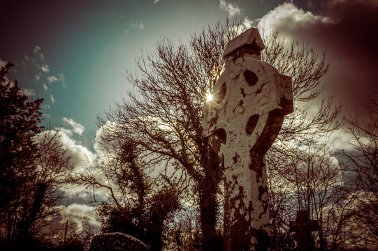 Old stone celtic cross with cloudy sky and dry tree
