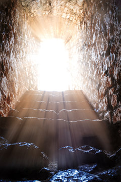 Resurrection of Jesus Christ. Religious Easter background, with strong light rays shining through the entrance into the empty stone tomb. 