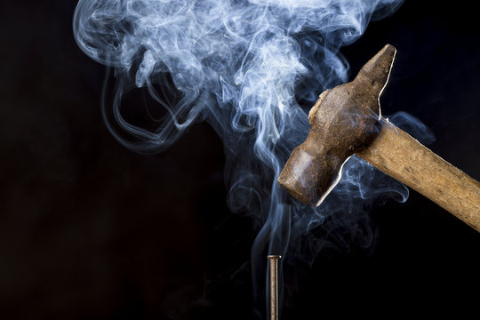 Abstract photo of metal rusty hammer above nail with smoke on black background