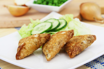 Three Indian samosas with green side salad on white plate on wooden surface
