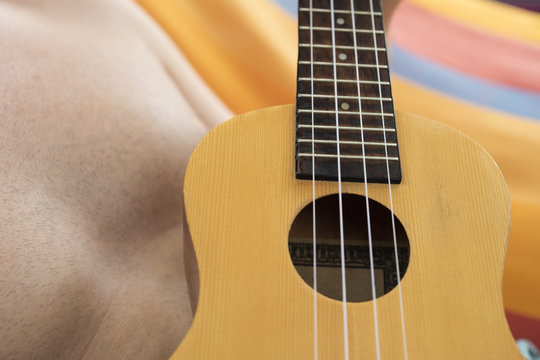 Detail of man relaxing on a hammock and playing ukulele