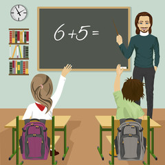 male teacher writing mathematic task on green chalkboard in classroom and children raising hands up
