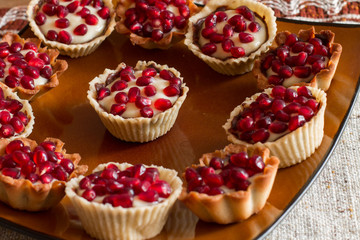 Tartletes with custard and pomegranate in big brown plate on linen tablecloth.