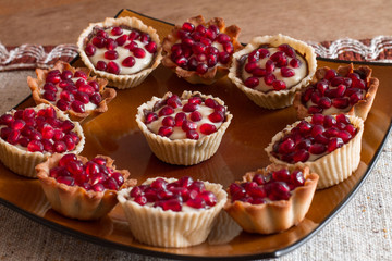Tartletes with custard and pomegranate in big brown plate on linen tablecloth.