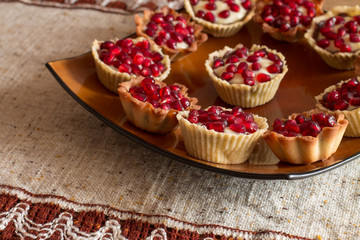 Tartletes with custard and pomegranate in big brown plate on linen tablecloth.