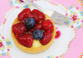 Crunchy tartelette with custard, fresh raspberries and blueberries on pink plate
