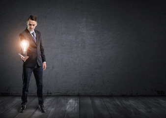 Obraz premium Front view of businessman standing and holding glowing light bulb in his hand