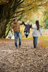 Lovely family walking in the autumn forest. Happy parents enjoying fresh air and beautiful nature, holding hands, talking, smiling and laughing. Healthy lifestyle
