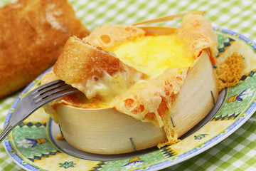 Piece of French bread dipped into baked cheese, close up
