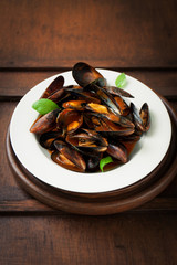 Homemade cooked mussels with garlic, tomato sauce, italian herbs, white wine and fresh basil in a plate, closeup
