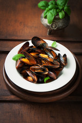 Homemade cooked mussels with garlic, tomato sauce, italian herbs, white wine and fresh basil in a plate, closeup, selective focus