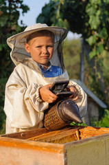 beekeeper portrait of a young boy who works in the apiary at hive with smoker for bees in hand