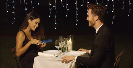 Gorgeous young woman opening a surprise gift from a young man during a romantic dinner for two at a restaurant
