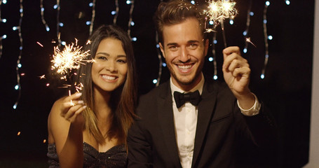 Elegant romantic young couple celebrating new year with sparklers laughing and smiling against a...