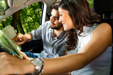 Happy young couple with a map in the car. They are using map on road trip.
