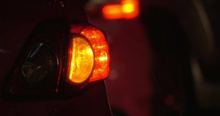 Close-up shot of car with switched on backlight and hazard lamp under the rain at night