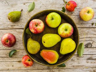 Fresh and ripe pears and apples in old plate on rustic wooden background.