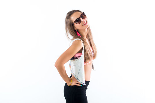 Young female model standing sideways, bending her body, putting arm on hip, wearing sunglasses and bright accessories.