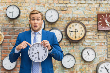 Man in suit standing near wall with clocks