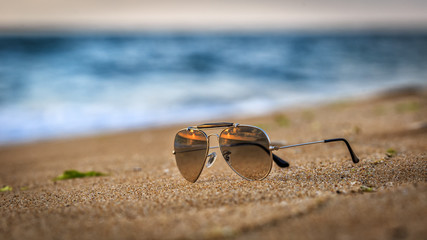 Fototapeta na wymiar Sunglasses on the beach with sunrise reflections