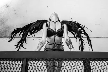 Wall murals Female Top view black and white photo of beautiful seductive angel woman wearing lingerie and leather belts on the roof over white wall