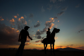 Silhouette of a horse with man teaching woman to ride at sunset
