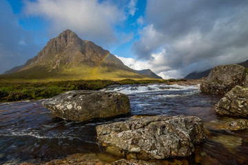 Beautiful river with rocks in it flowing in a scottish Valley next to a huge mountain in the background.