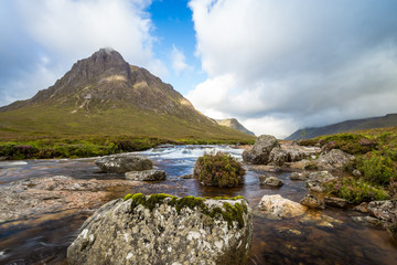Beautiful river with rocks in it flowing in a scottish Valley next to a huge mountain in the background.