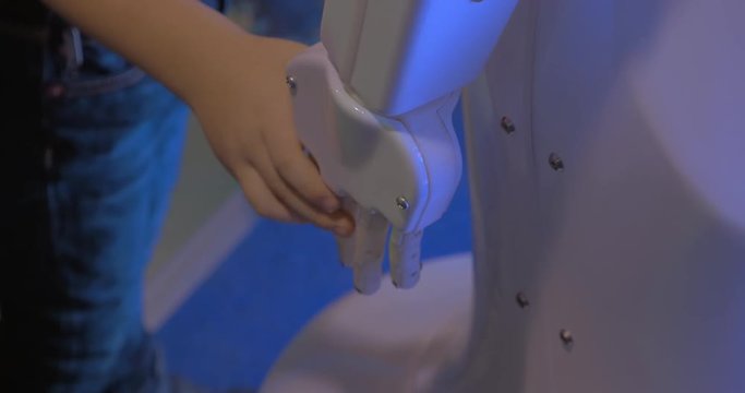 Close up view of small boy hand holds white plastic hand of humanoid robot in Robotics exhibition and conference ECC Sokolniki. Moscow, Russia