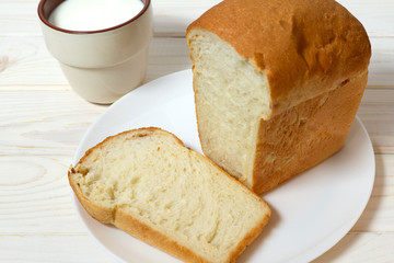 A loaf of white bread on a plate and a cup of milk