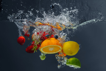 Different fruits and berries falling in water on dark background