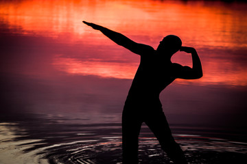 Mężczyzna nad jeziorem ćwiczy jogę, w tle zachód słońca