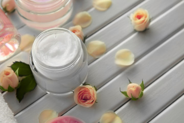 Composition with cosmetic cream and roses on wooden background