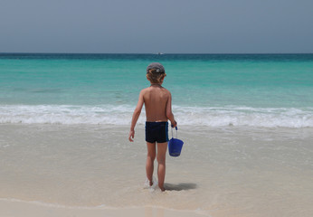 Fototapeta na wymiar Мальчик с ведерком в руке идет купаться в море