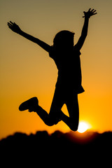 Dziewczynka skacząca z radości na tle zachodzącego słońca