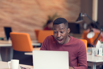 Young business man with a shocked expression working on a laptop