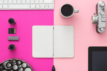 Designer's desk with coffee, scrapbook and retro camera. Feminine and elegant. Pink background. Directly above.